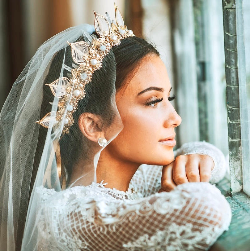 Bride looking out a window wearing a gold crown with moonstone and pearls