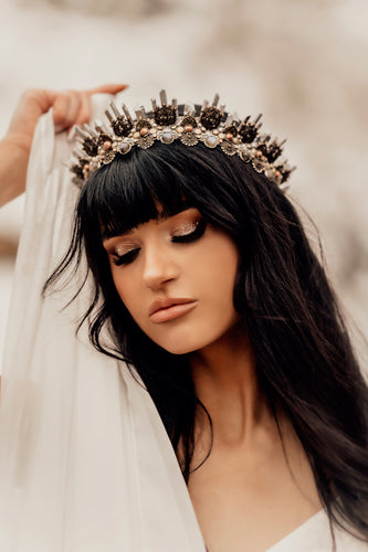 Dark haired beauty with thick black eyelashes in a white dress poses with Arianrhod crown on her head